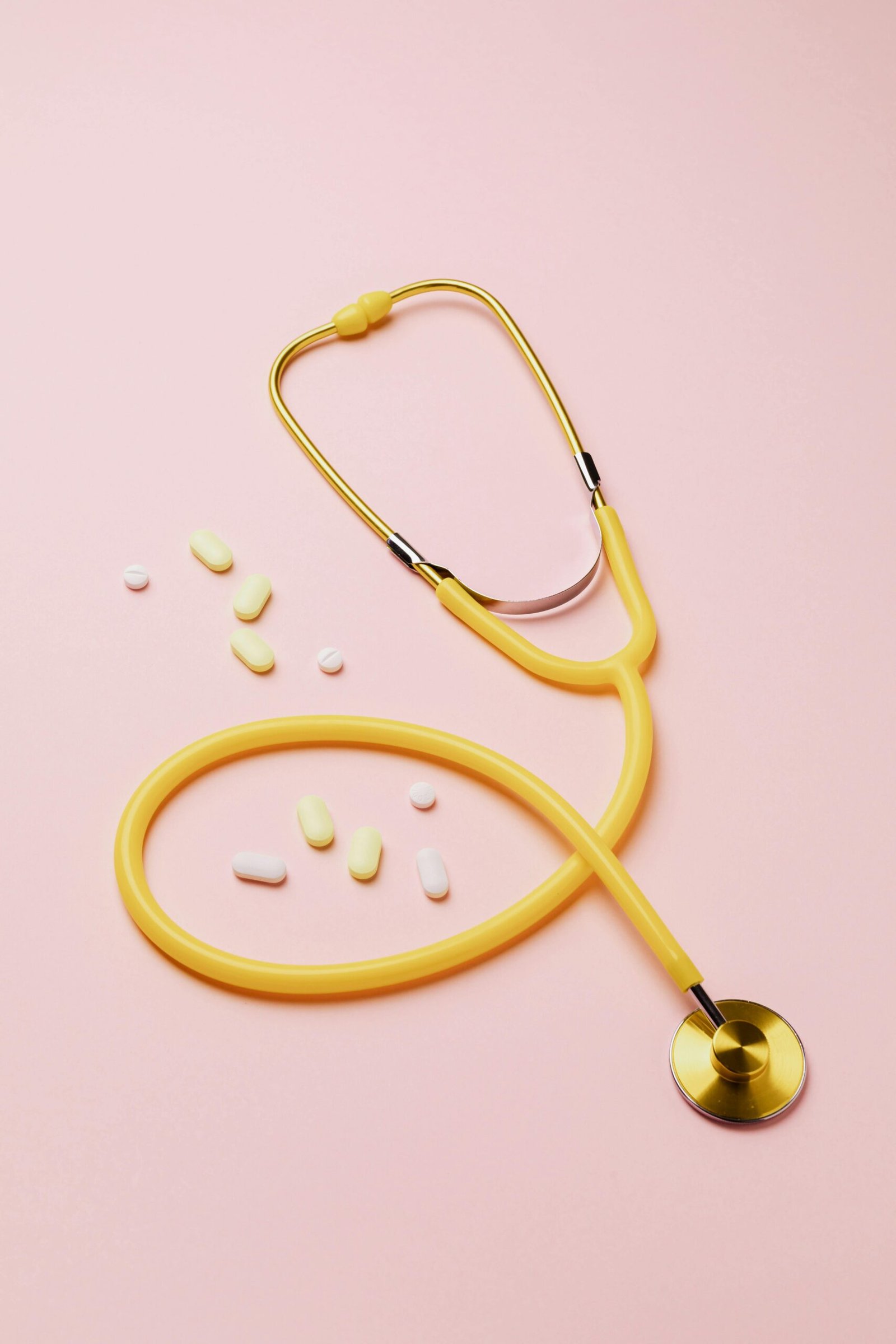 A yellow stethoscope and assorted pills on a pink background symbolize healthcare and treatment.